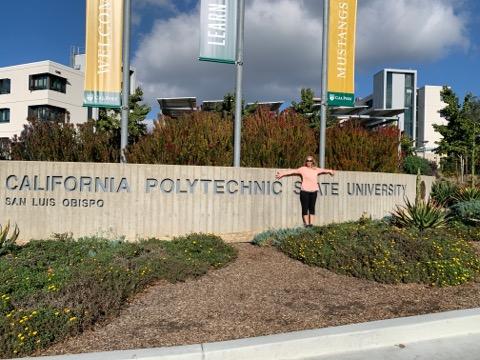 Kris at Cal Poly in front of the retaining wall with name of the college inscribed.