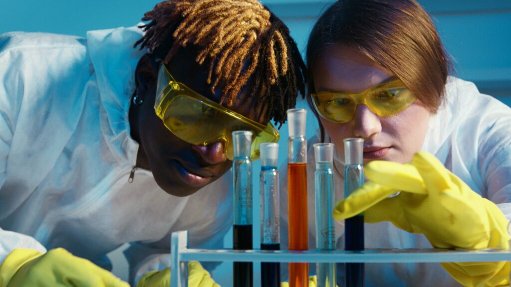 Two students in safety goggles looking at test tubes