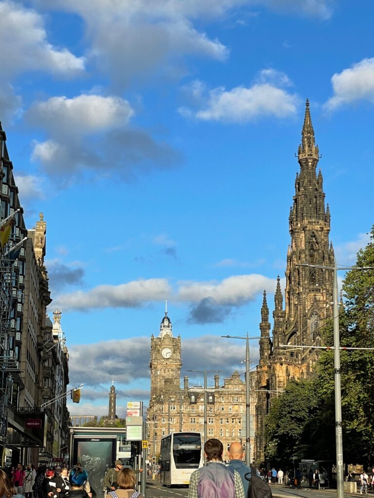 Princes Street - busy street with modern bus and centuries-old buildings with spires and clock,