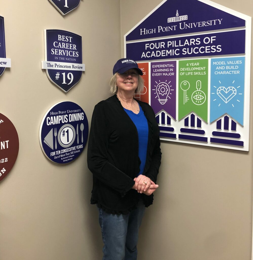 Sue posing by an HPU sign that shows Four Pillars of Academic Success