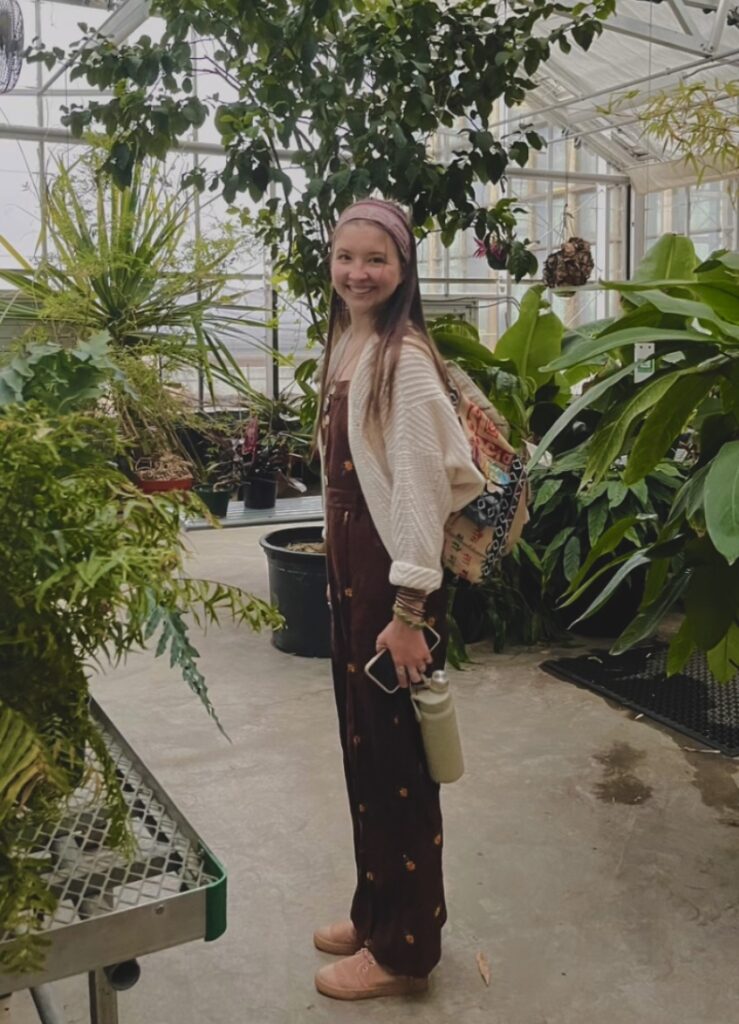 Smiling student dressed in pink surrounded by plants in St. Olaf greenhouse