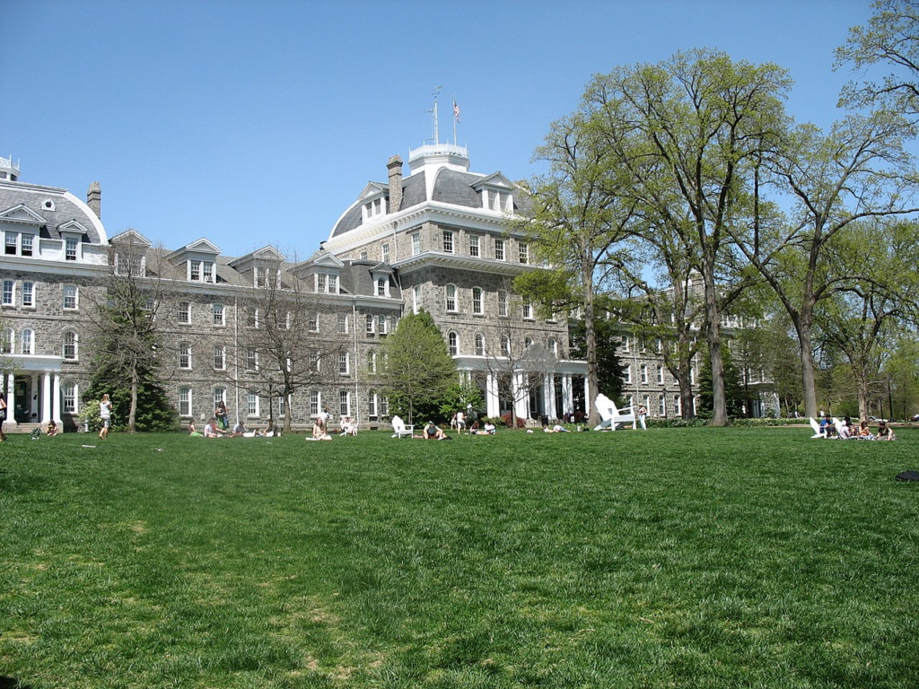 Large historic gray-brink building on green lawn with white Adirondack chairs