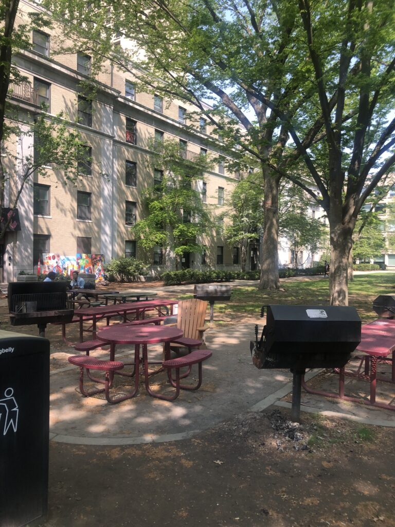 Patio in front of brick residence halls with red tables and barbeque.