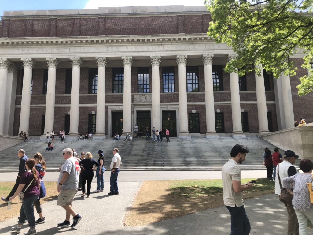 Students and visitors passing by steps of Widener Library on a sunny day