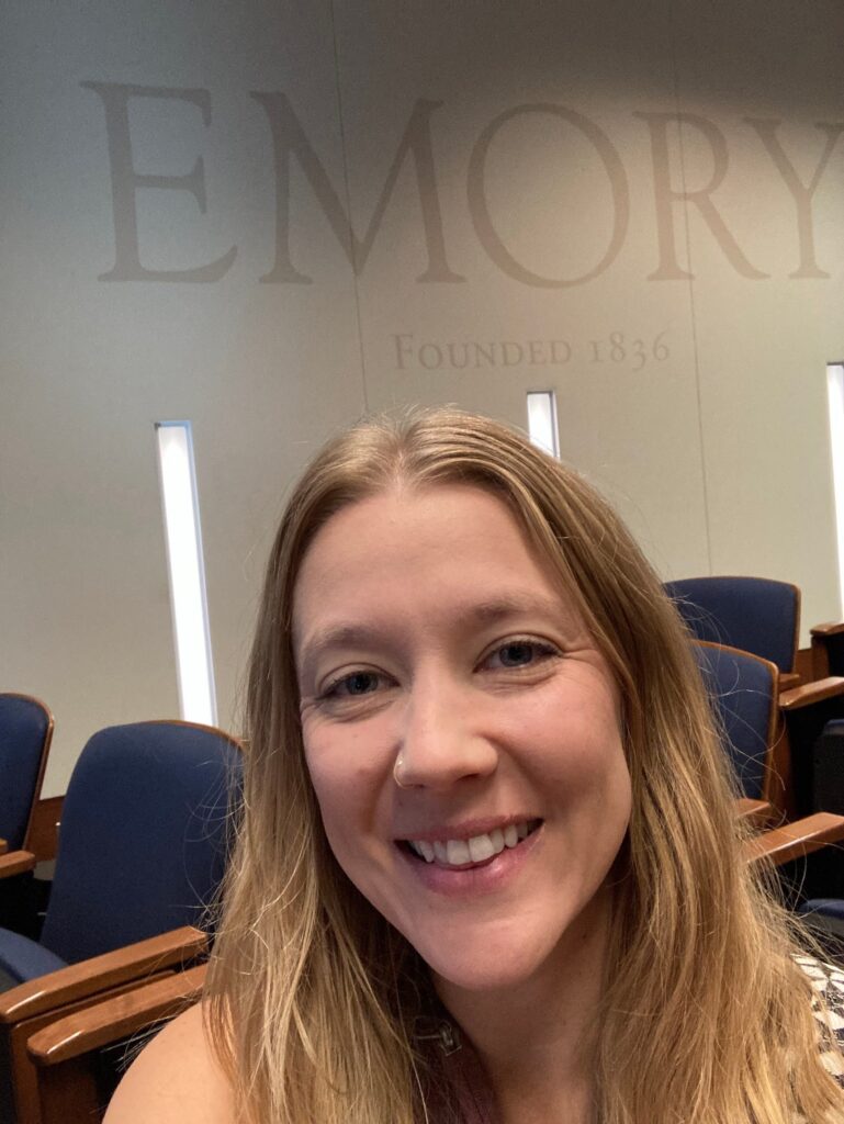 Author smiling in front of Emory signage