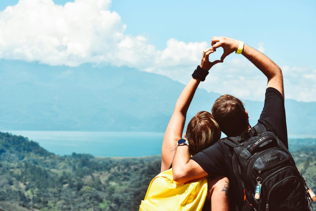 Backs of two students in front of nature landscape doing heart hands